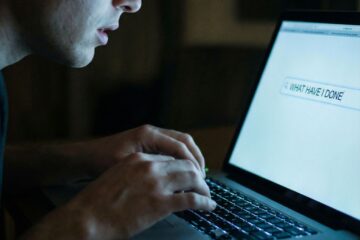 노트북 화면의 빛나는 검색창에 문장을 입력하는 손과 얼굴이 부드럽게 비친 클로즈업 모습이다